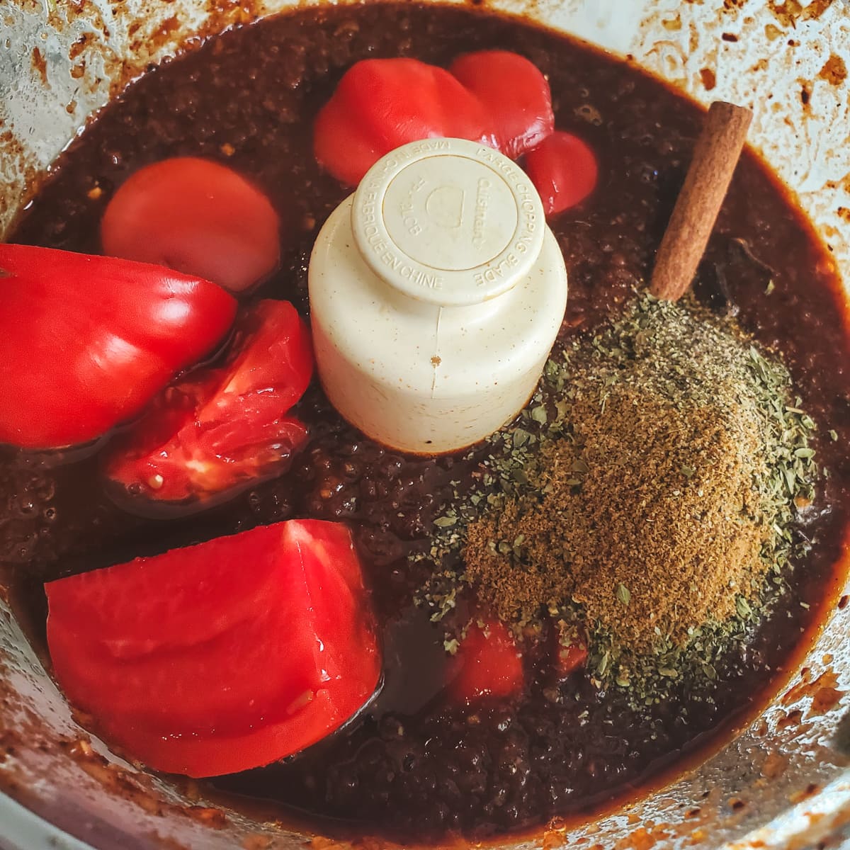 Tomatoes and spices added to a sauce in a food processor.