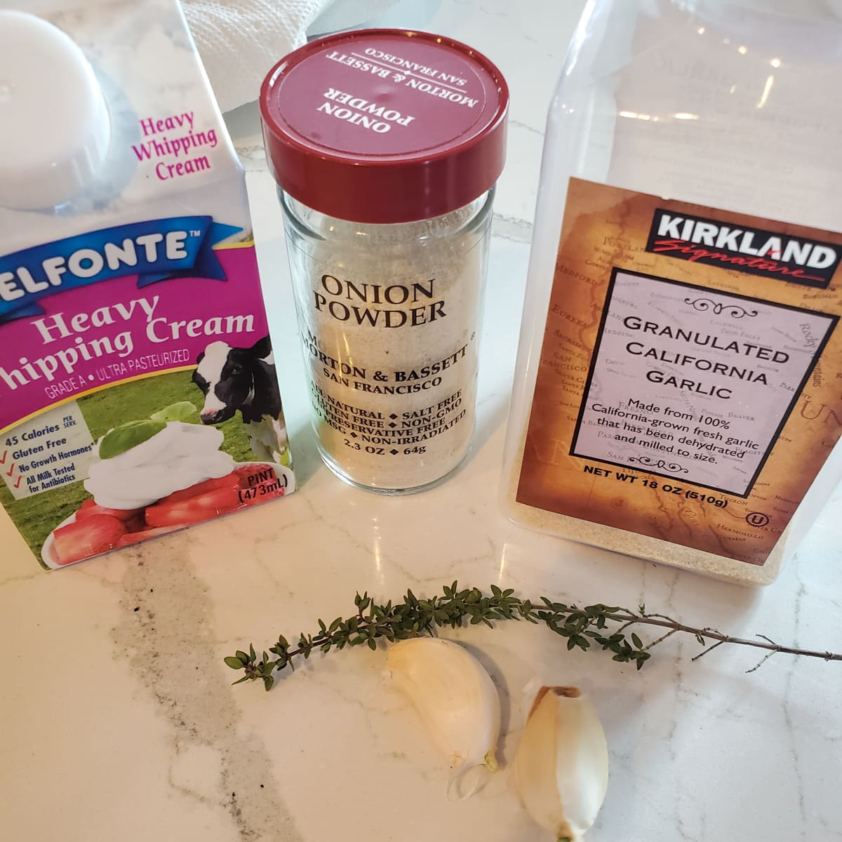 Heavy cream, thyme, garlic, onion powder, and garlic powder on a countertop.