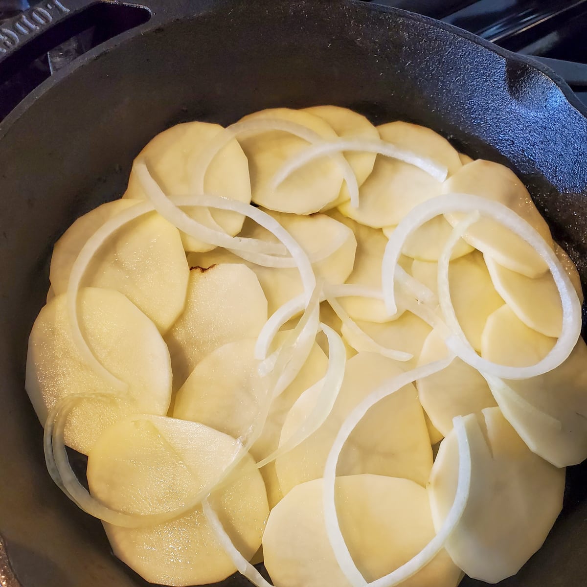 Potato and onion slices layers in a cast iron pan.