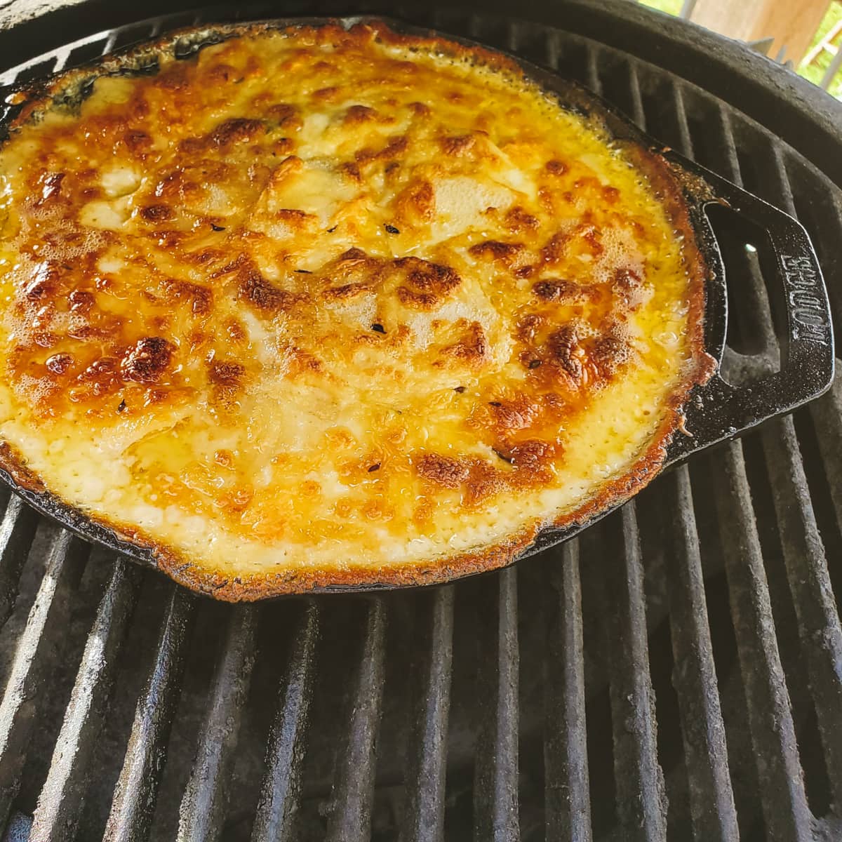 Smoked au gratin potatoes in a cast iron pan cooking on a Big Green Egg smoker.