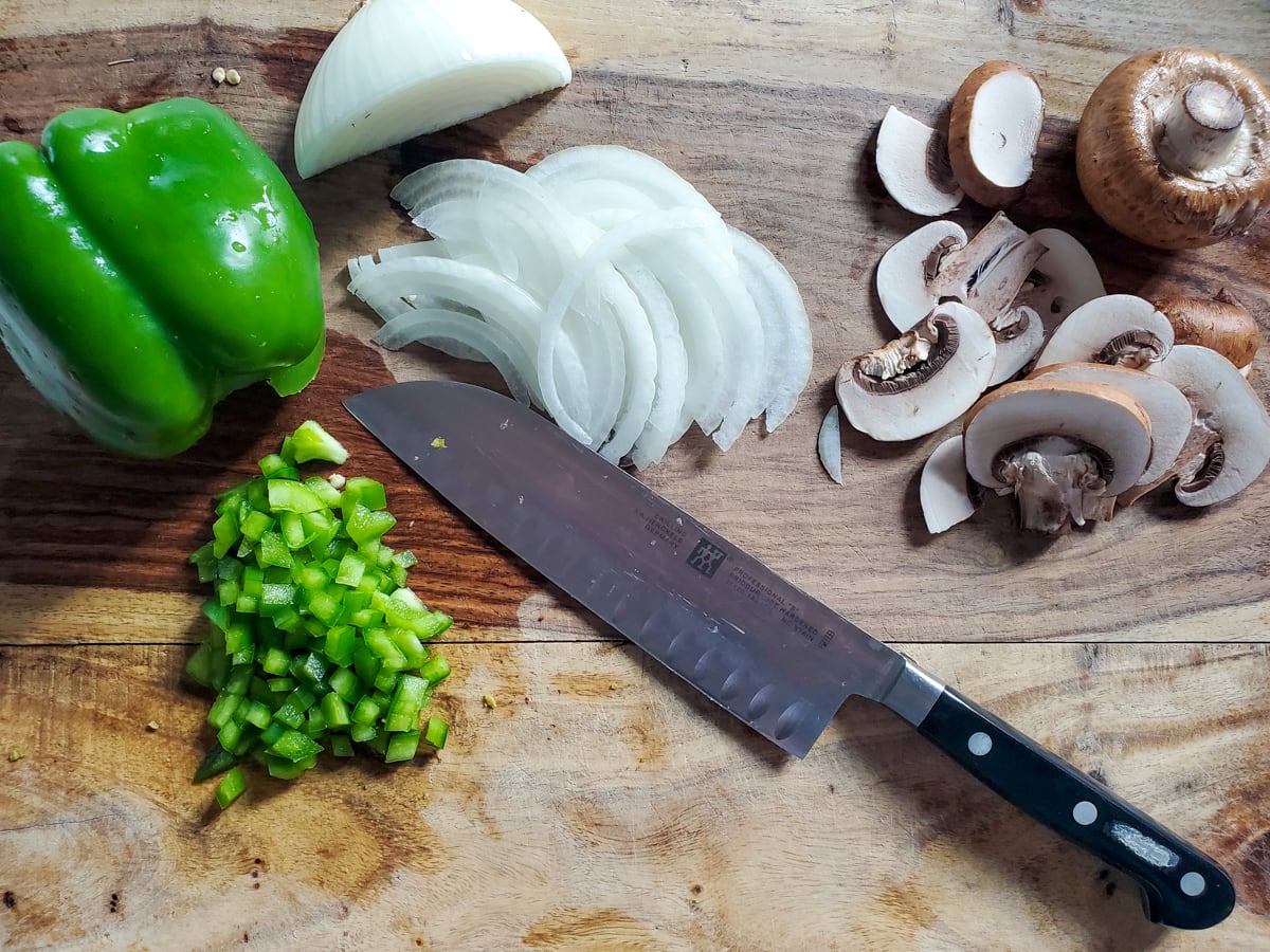 Sliced onion, mushrooms, and diced bell pepper on a cutting board.
