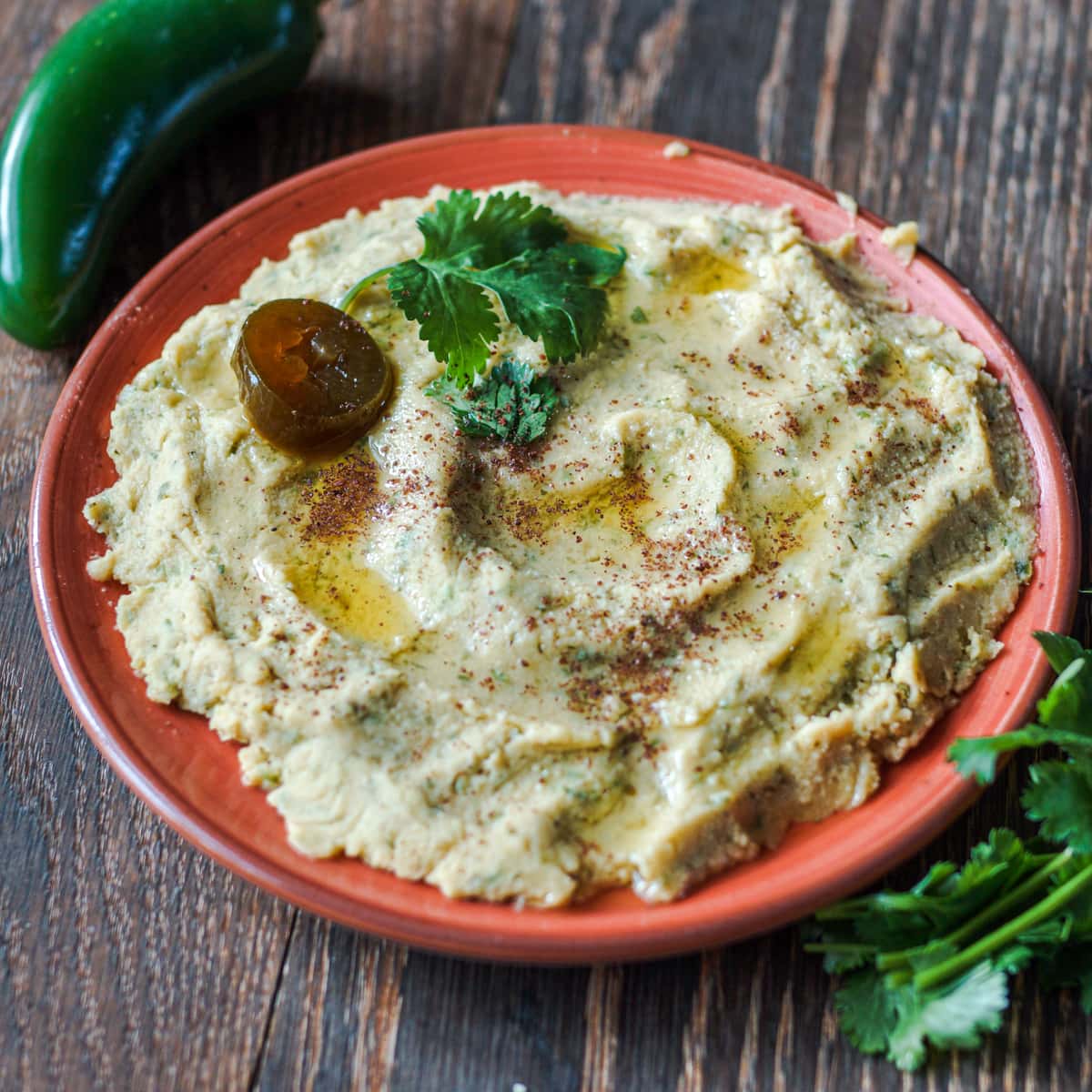 Smoked humus with jalapeno and cilantro on a wood table.