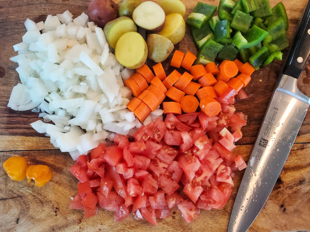 Diced tomatoes, onion, bell peppers, carrots, and potatoes on a cutting board,