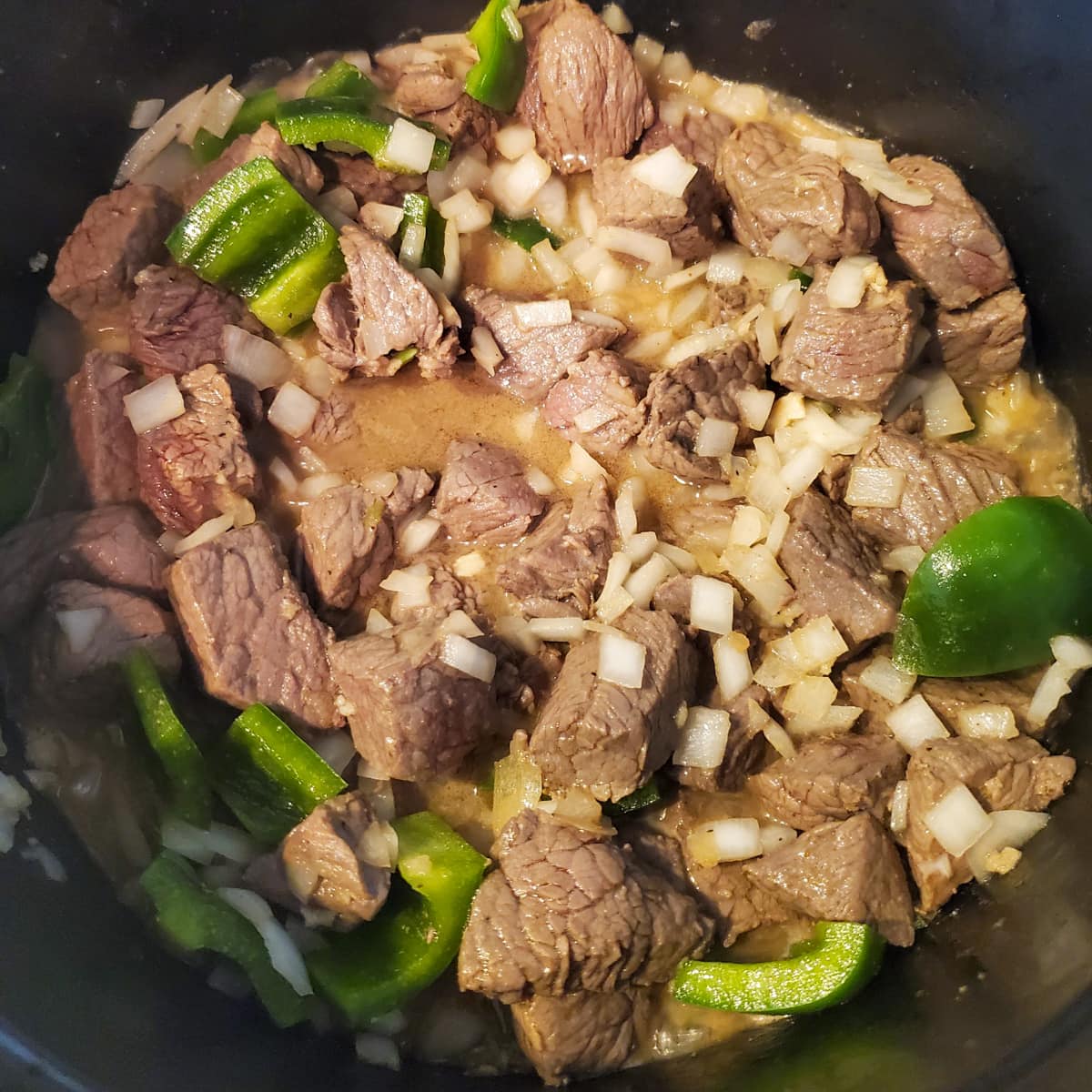 Vegetables added to stewed beef in a Dutch oven.