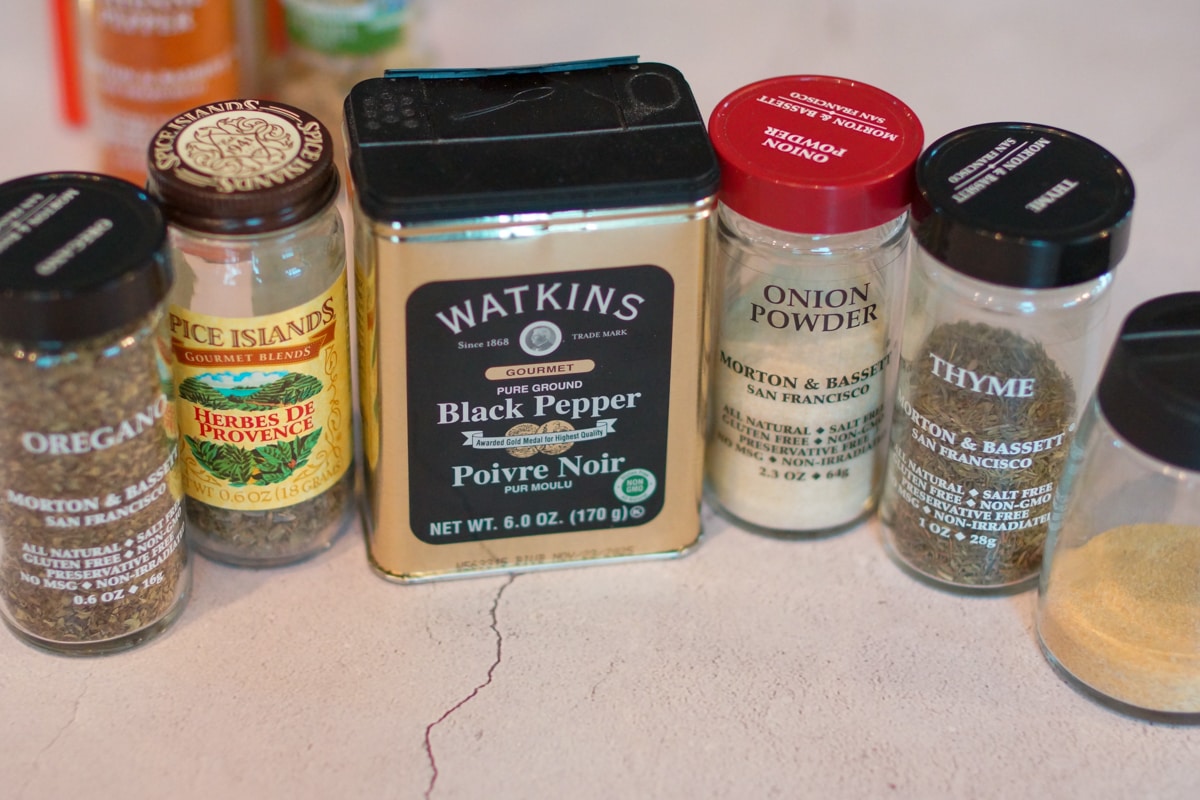 Onion powder, black pepper, thyme, and herbes de Provence on a countertop.