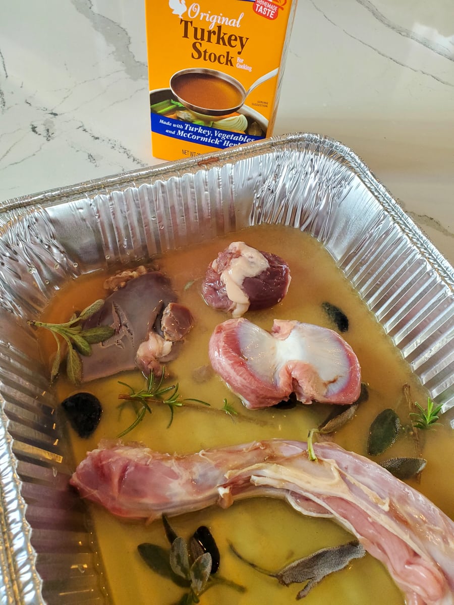 Turkey neck and giblets in a foil pan with turkey stock and herbs.