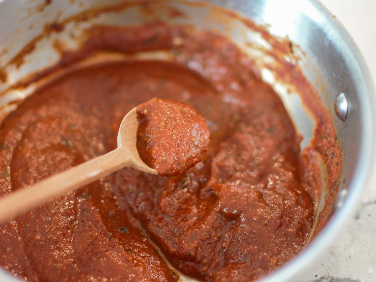 Pizza sauce with red wine being stirred with a wooden spoon.