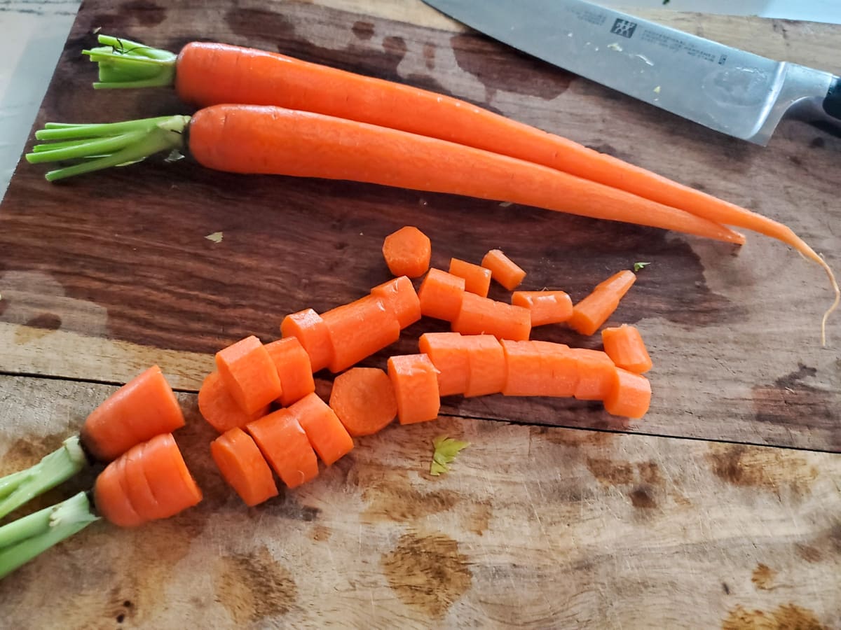 Carrots being cut into chunks on a wood cutting board.