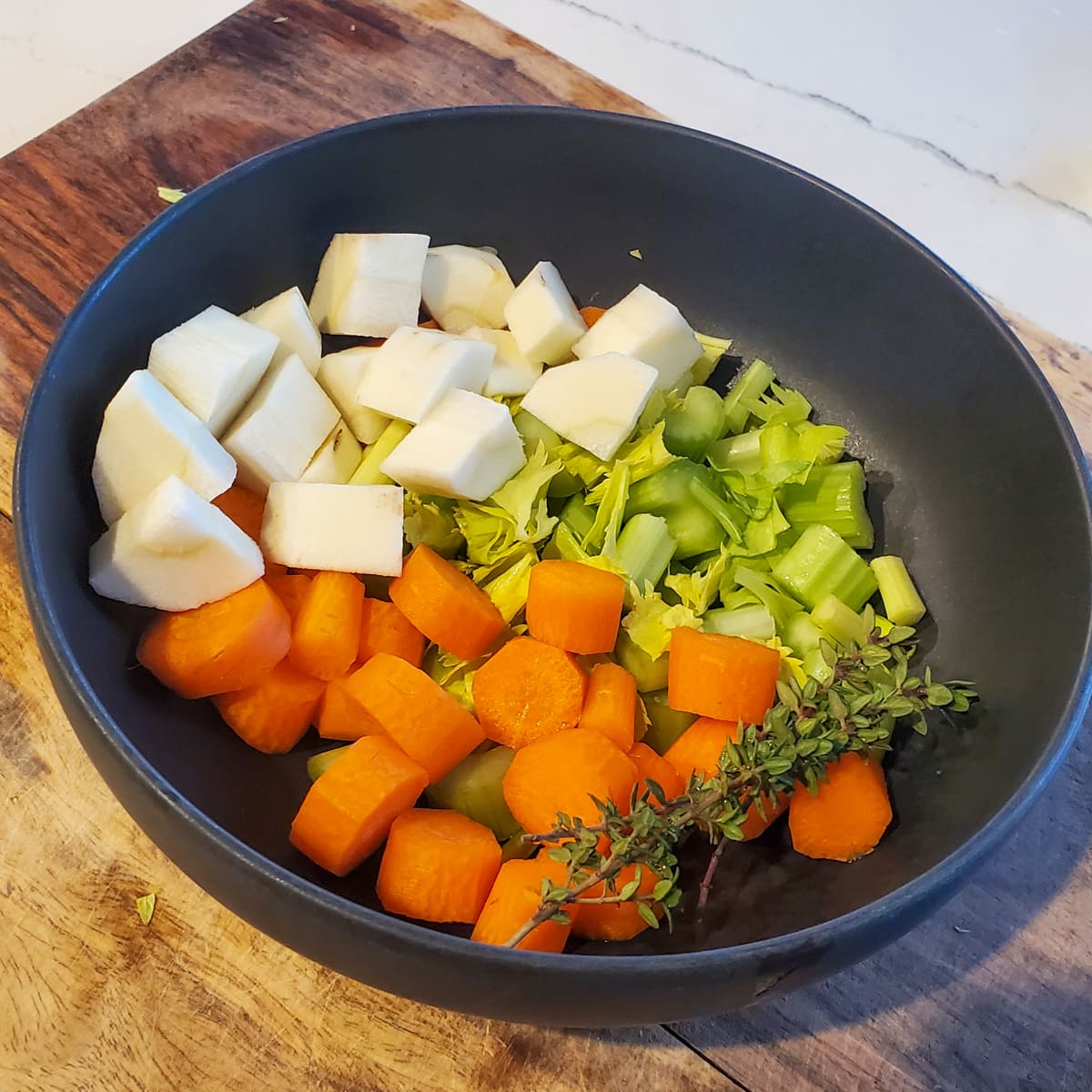 Cut carrot, parsnip, celery, and onion in a black bowl.