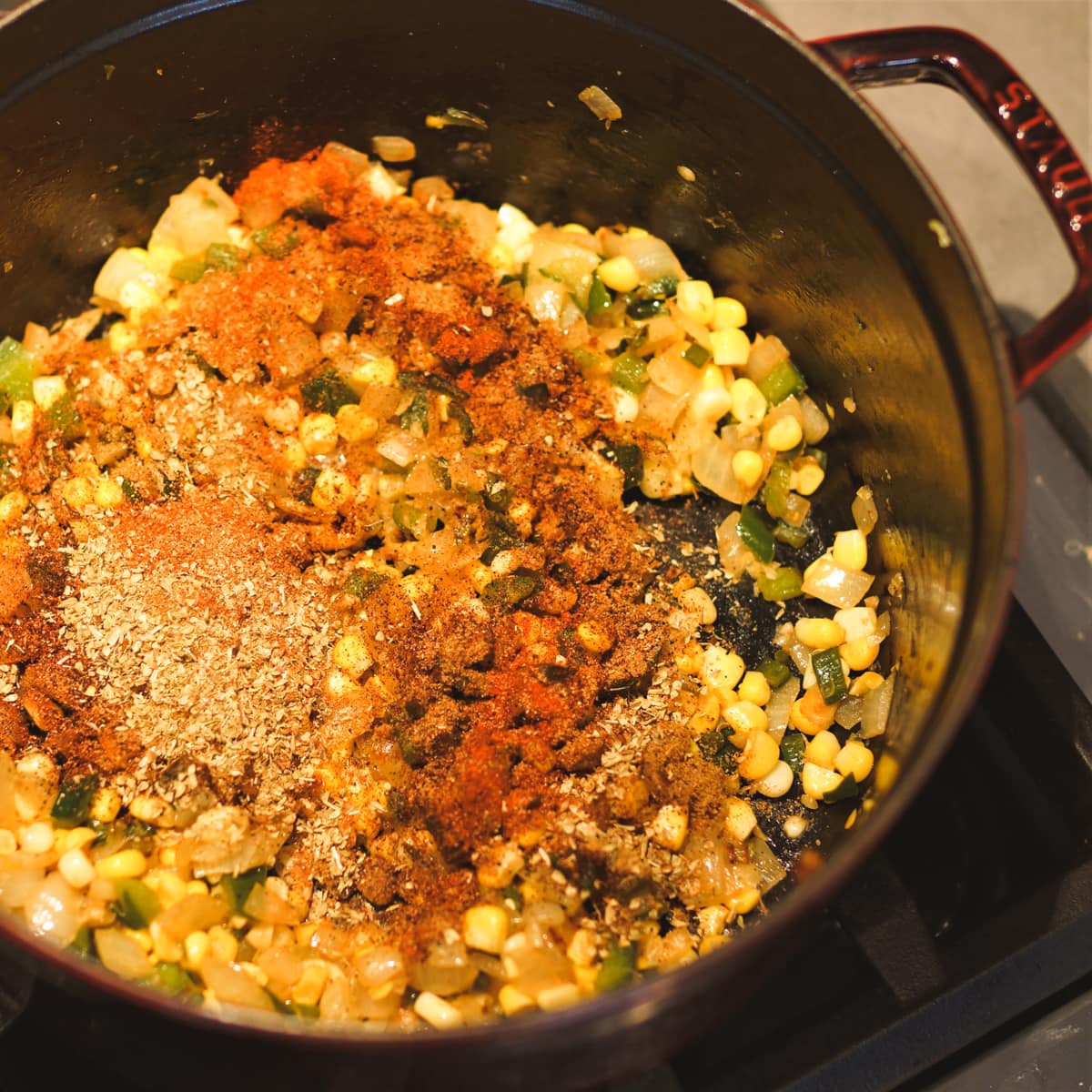 Corn and seasoning added to a Dutch oven of chicken chili.