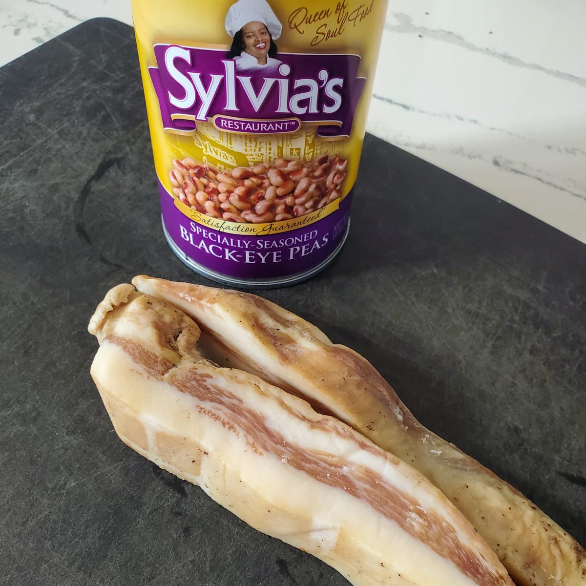 Can of black-eyed peas and guanciale on a cutting board.