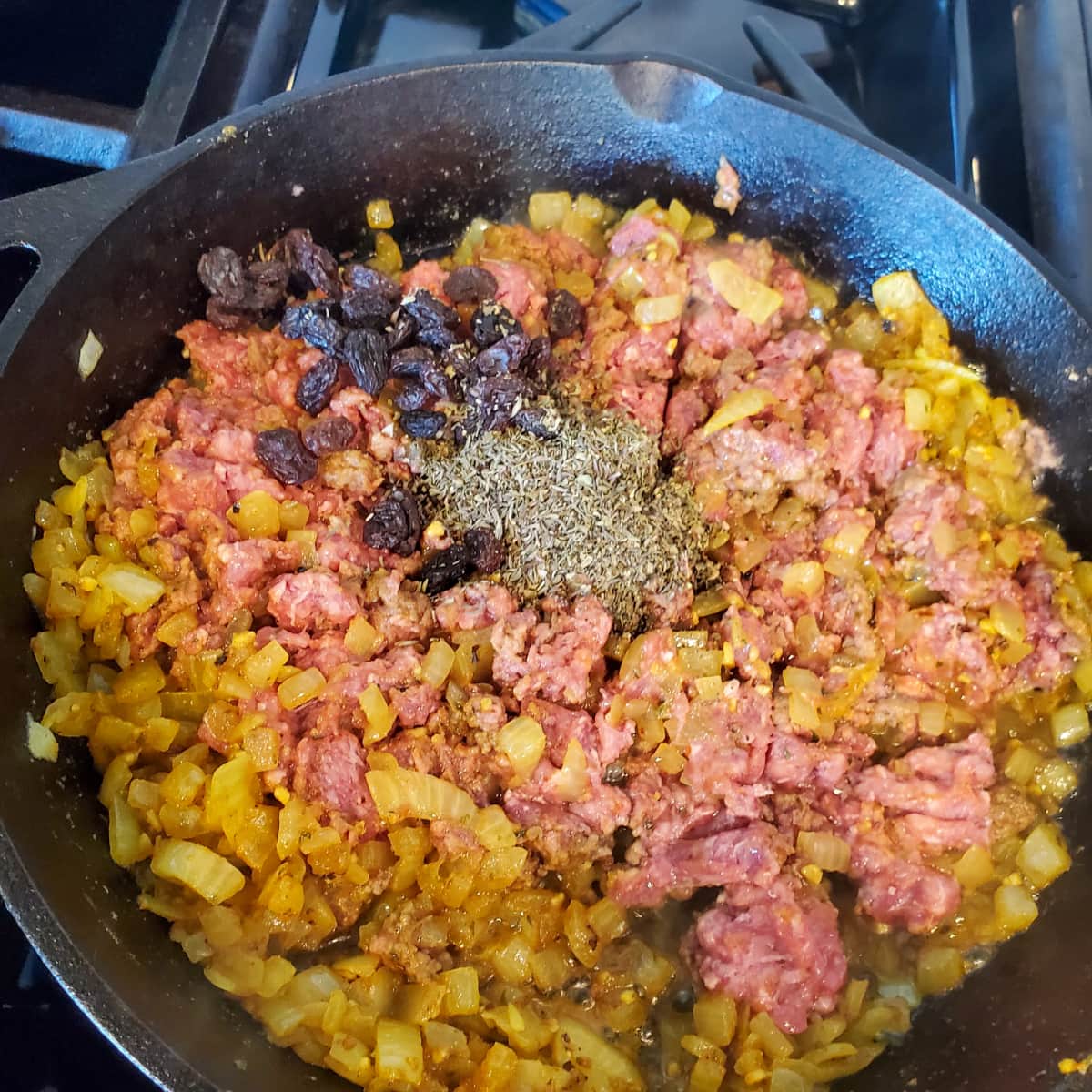 Raisins and herbs added to a pan of curried ground beef.