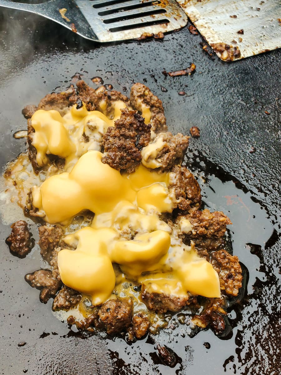 Chopped cheese sandwich with American cheese cooking on a Blackstone griddle.