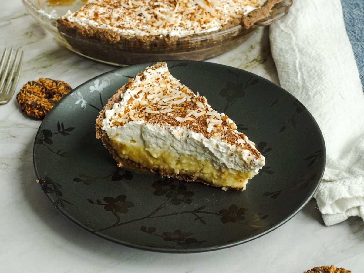 Slice of coconut cream pie, topped with toasted coconut and chocolate.