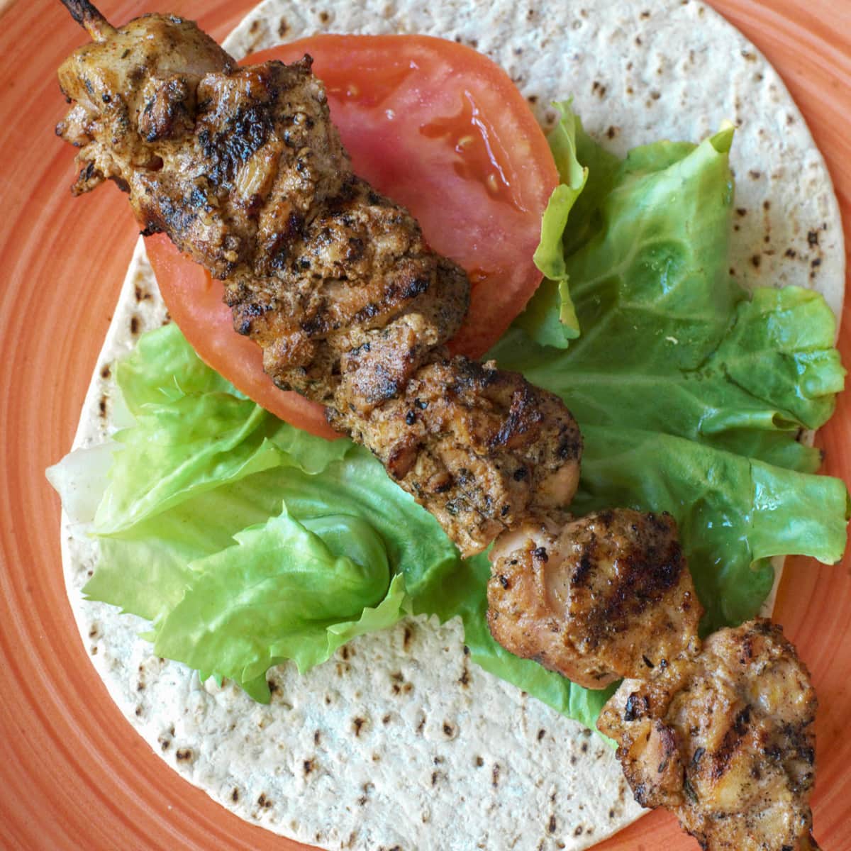 Grilled Shisk Taouk on a flatbread with lettuce and tomato.
