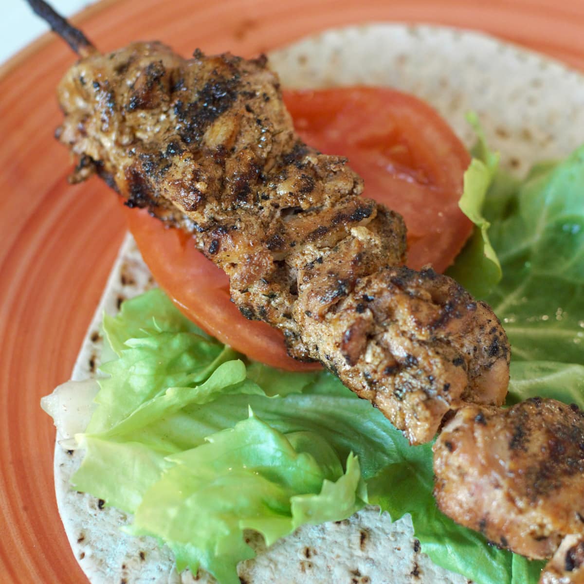 Grilled shish tawook kebabs served with flatbread, lettuce, and tomato.