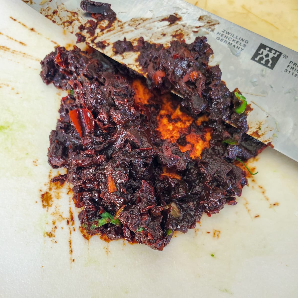 Spicy fermented bean paste being chopped on a cutting board.