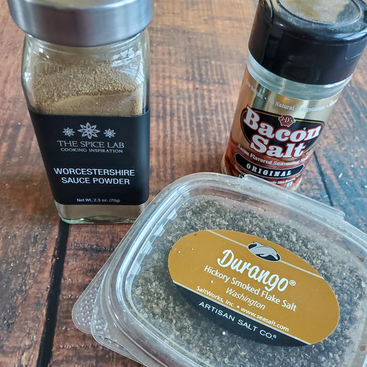 Worcestershire seasoning, bacon salt, and smoked salt on a wood table.