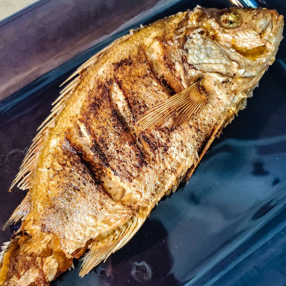 Fried whole snapper in a blue dish.