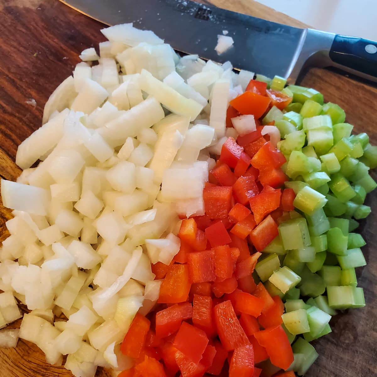Diced onion, celery, and red bell pepper on a cutting board.