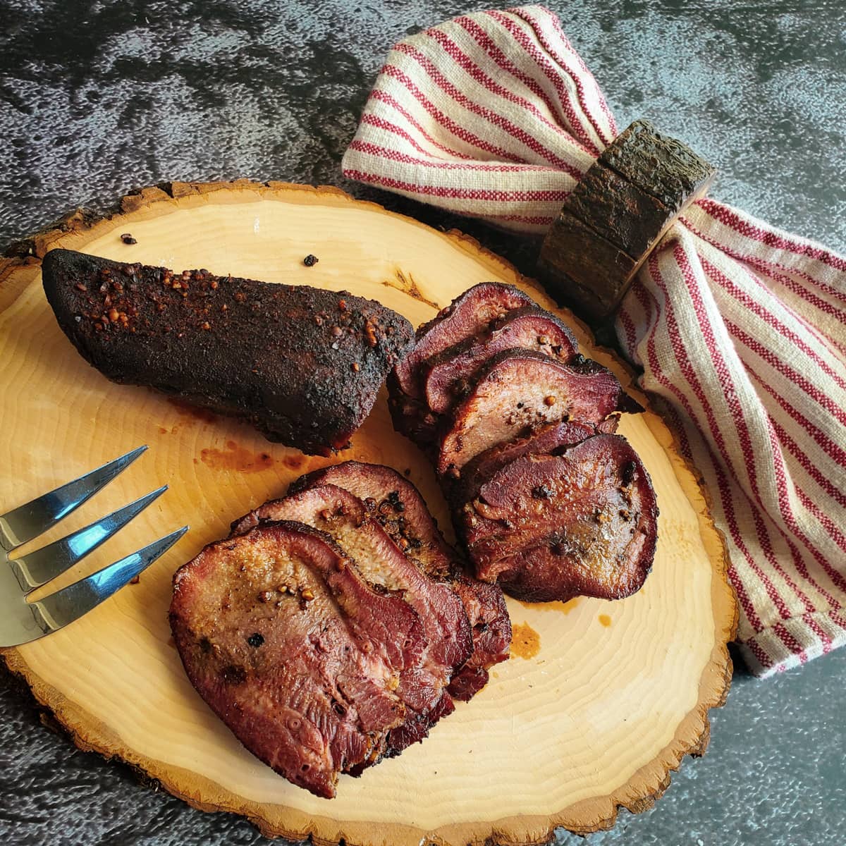 Smoked beef tongue pastrami cut into slices on a wood platter.