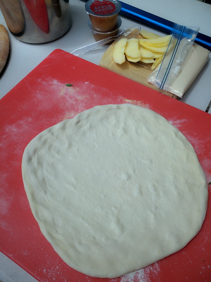 Pizza dough stretched out on a floured cutting board.