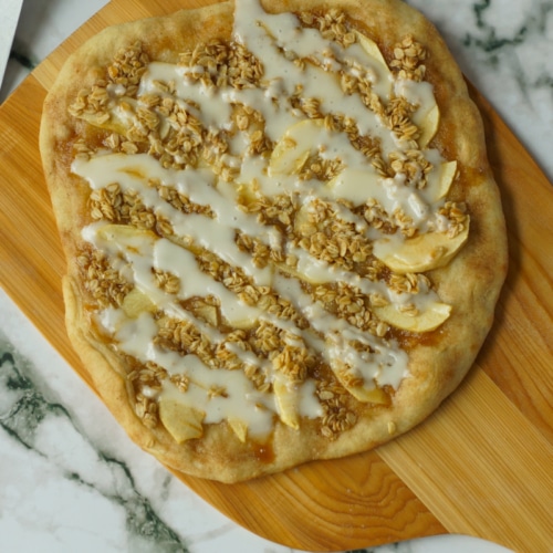 Dessert pizza topped with apple slices, applesauce, and cream cheese icing.