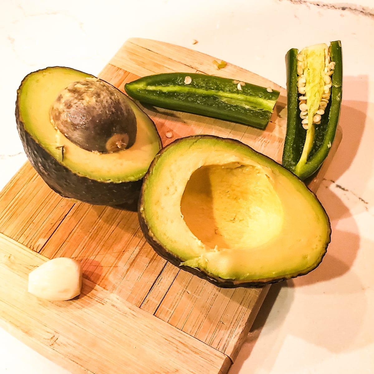 Halved avocado and jalapeno pepper on a cutting board.