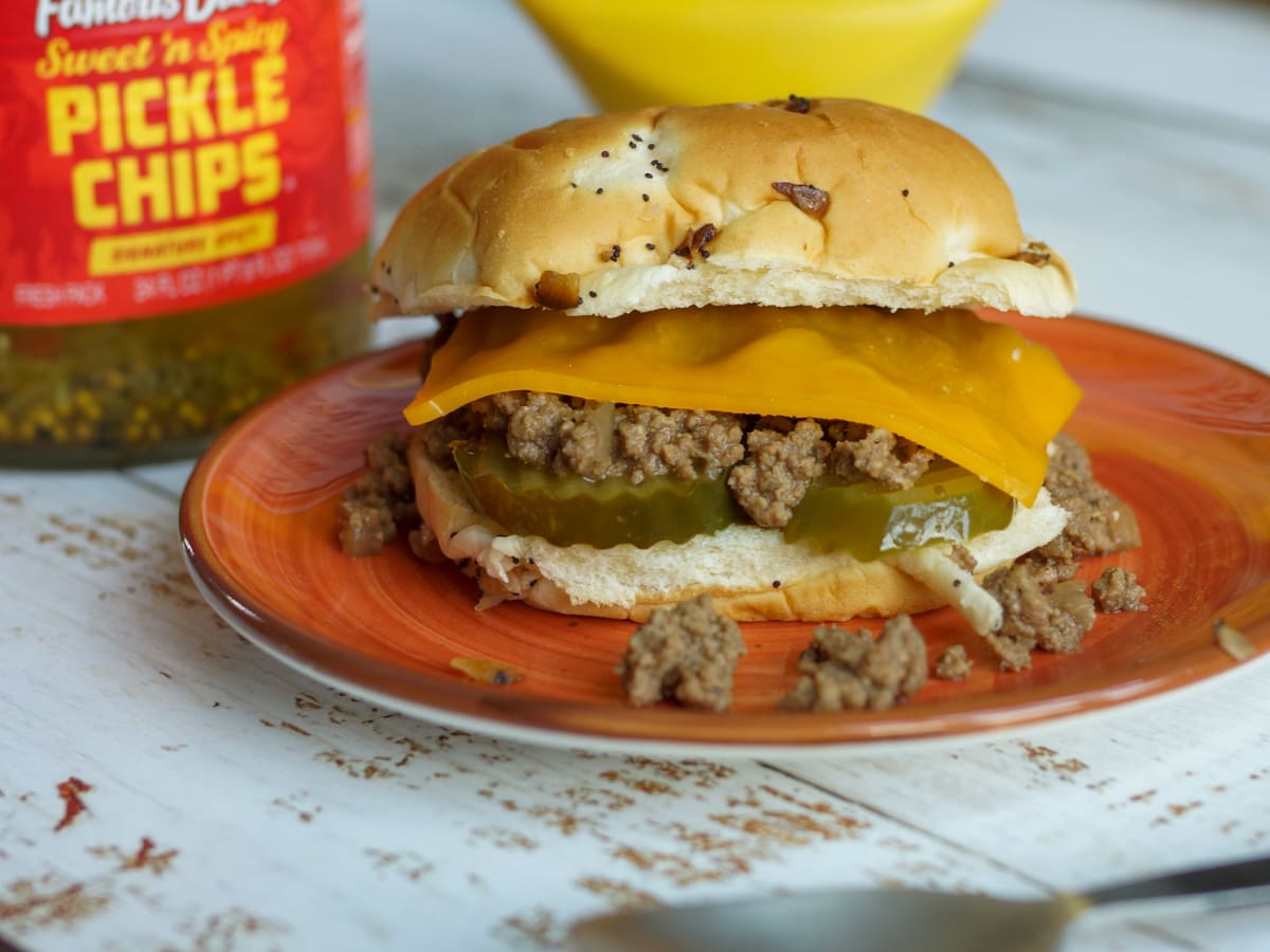 Dutch oven Iowa Style Maid Rite Loose Meat Sandwich topped with cheese and pickles.