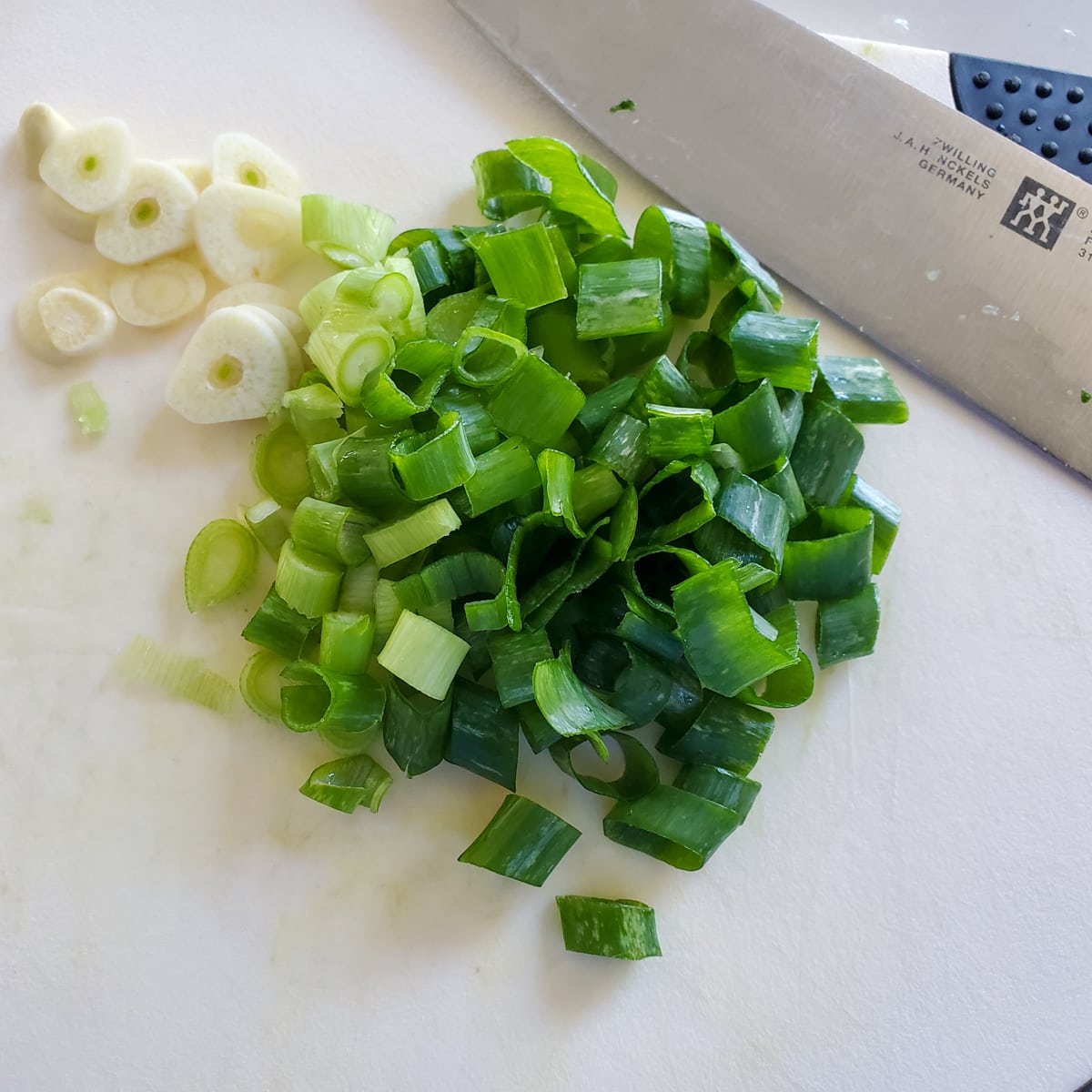 Chopped green onion and sliced garlic on a cutting board.