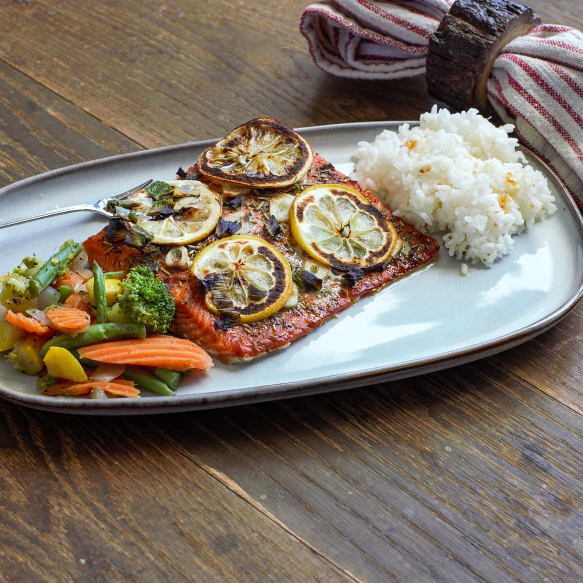 Ooni wood plank salmon on a wood table, served with rice and vegetables.