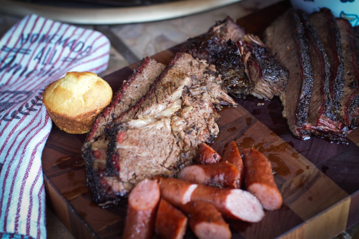 Smoked Texas Brisket on a cutting board with sliced sausage and BBQ sides.