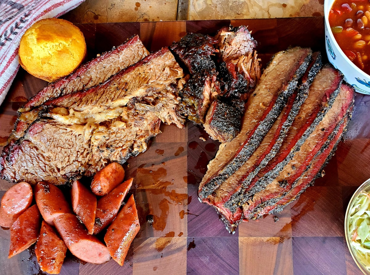 Texas style brisket in a cutting board with sausage and cornbread.