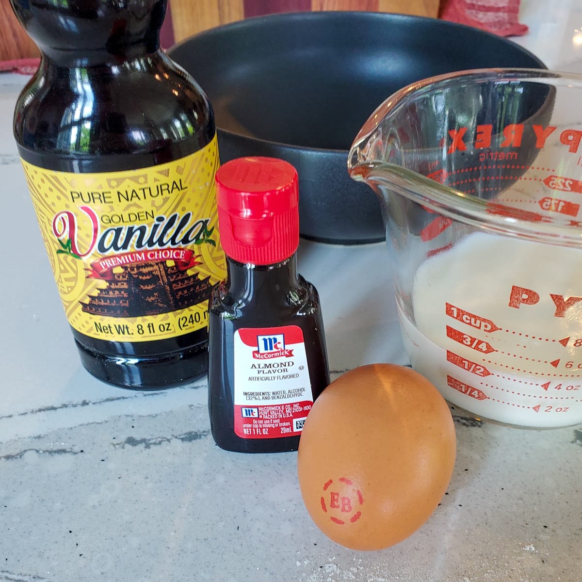 Vanilla, egg, milk, and almond extract on a countertop.