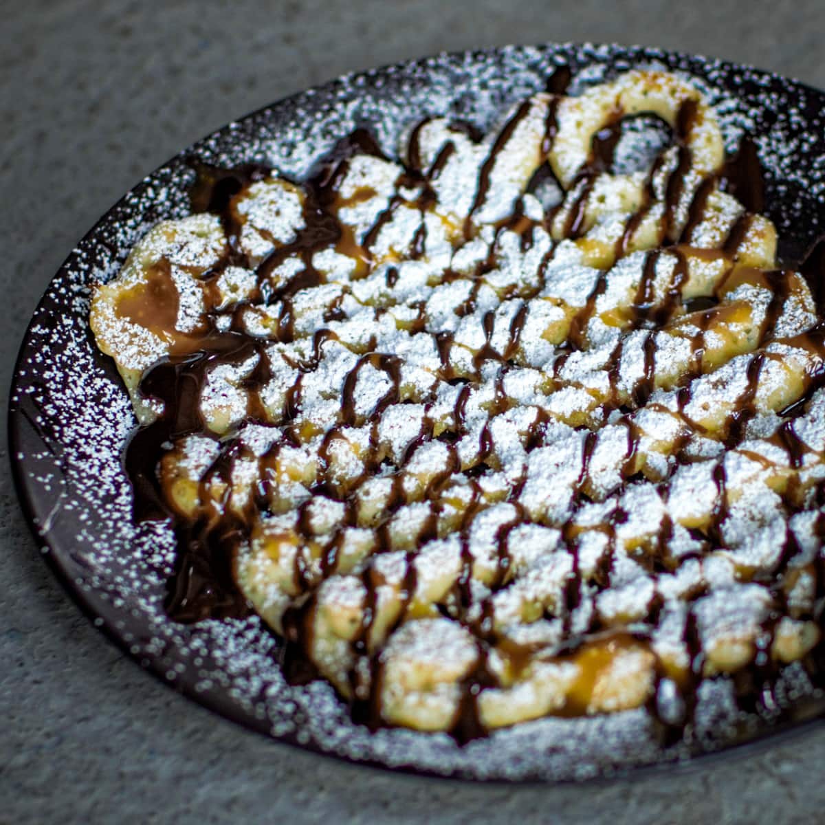 Fresh funnel cakes dusted with powdered sugar, and chocolate syrup.
