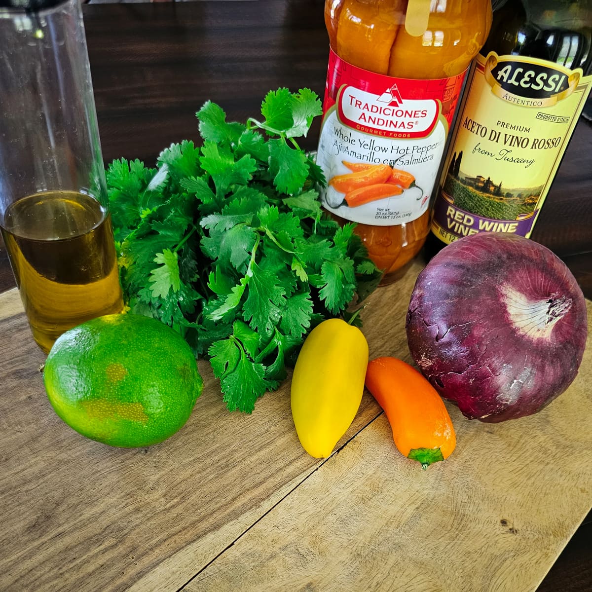 Lime, red onion, cilantro, red wine vinegar, olive oil, and Aji Amarillo peppers on a cutting board.