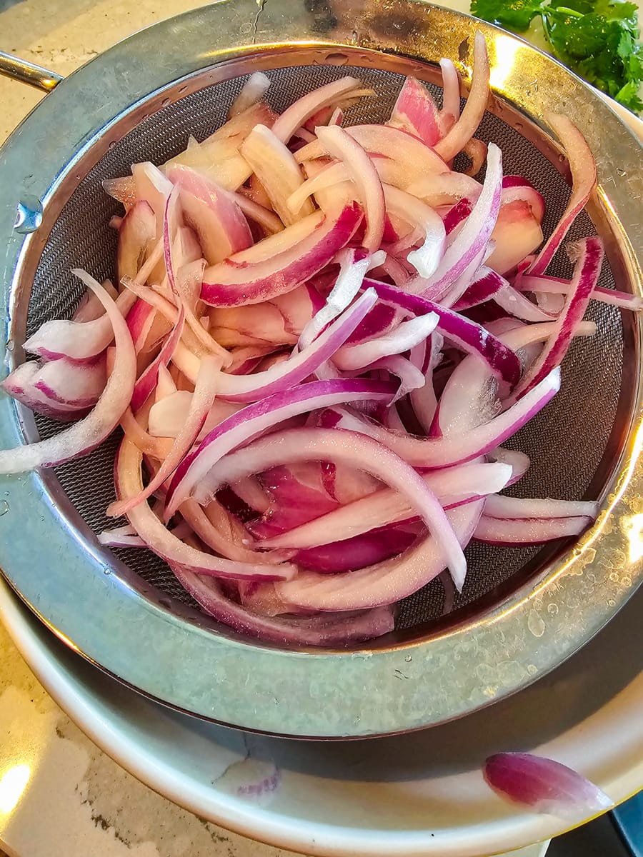 Red onion slices in a colander.