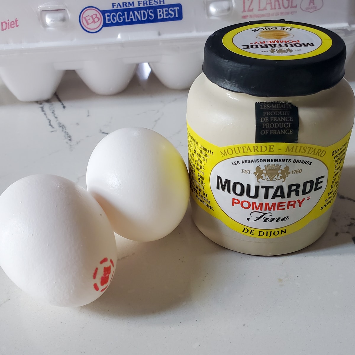 Two eggs and Dijon mustard on a granite countertop.