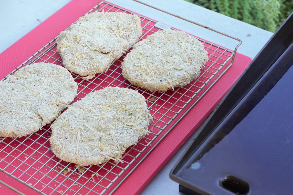 Breaded Italian butterfly pork chops, next to a Blackstone griddle.