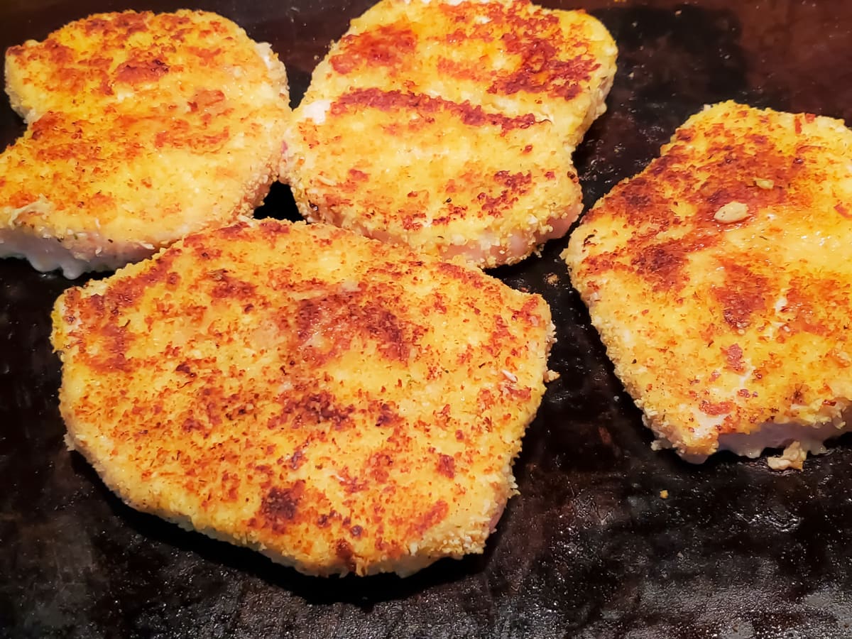 Breaded Italian pork chops cooking on a flattop griddle.