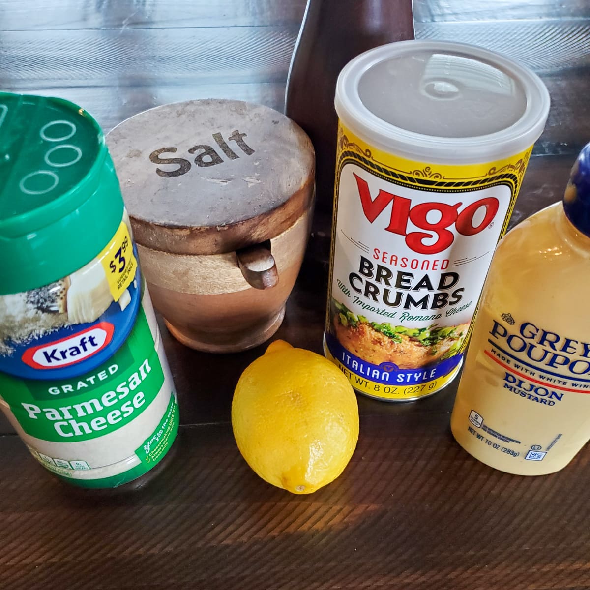 Parmesan salt, lemon, Dijon mustard, and Italian breadcrumbs on a countertop,