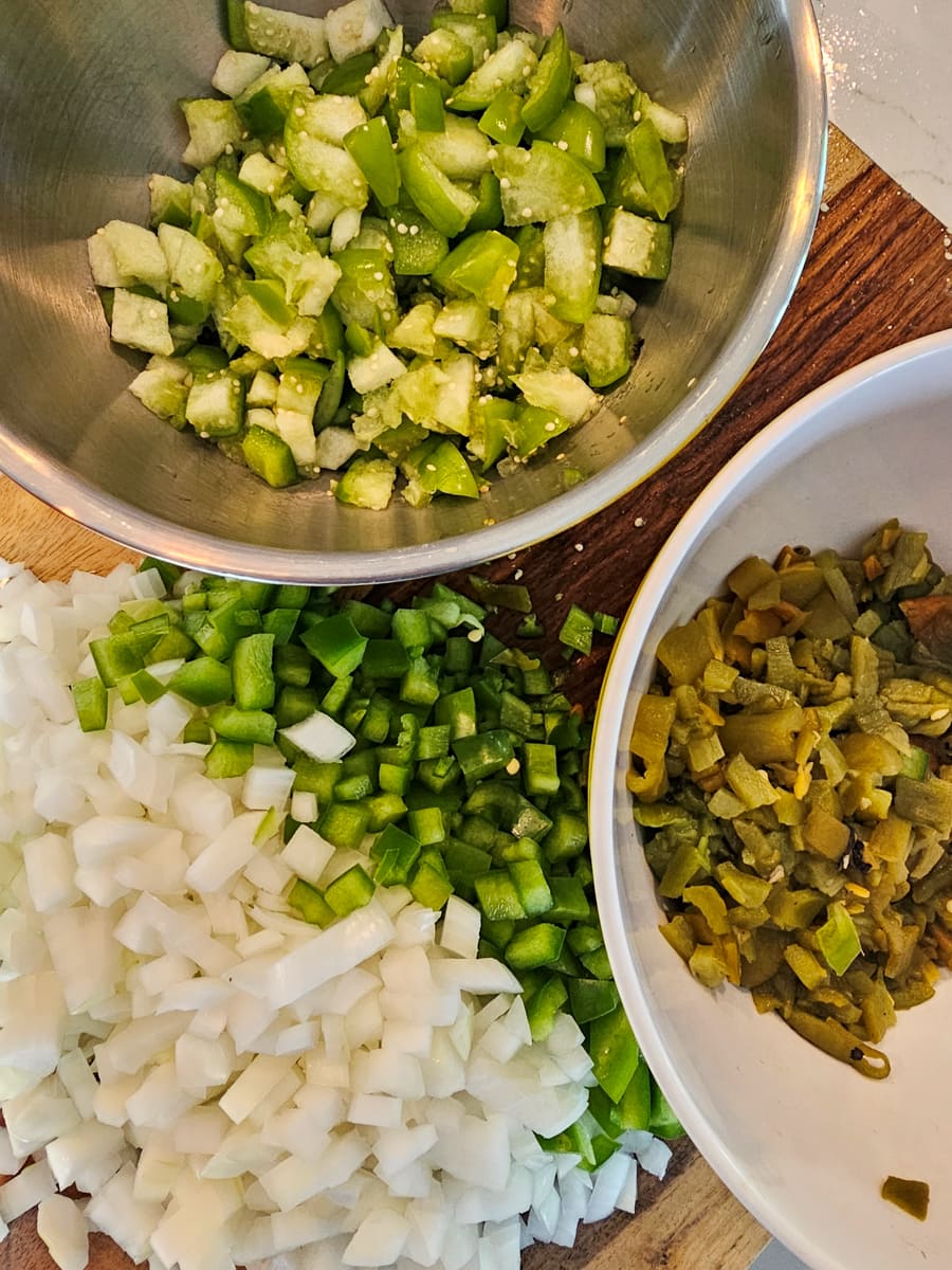 Diced onion, chiles, and tomatillos on a cutting board.