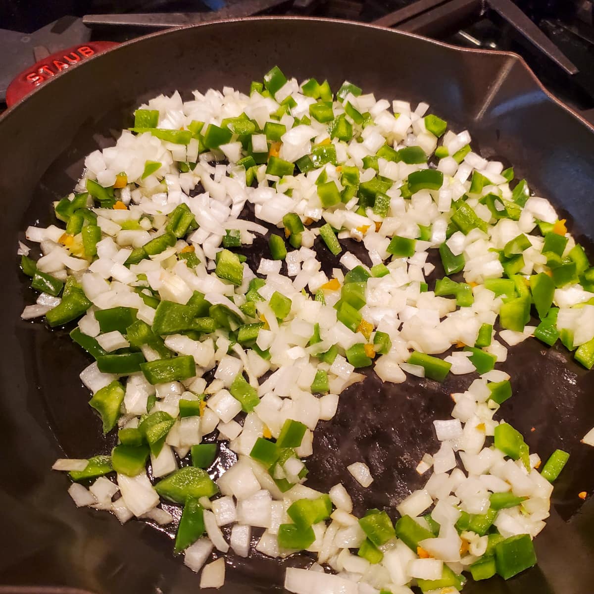 Onions and peppers sautéing in a cast iron pan.