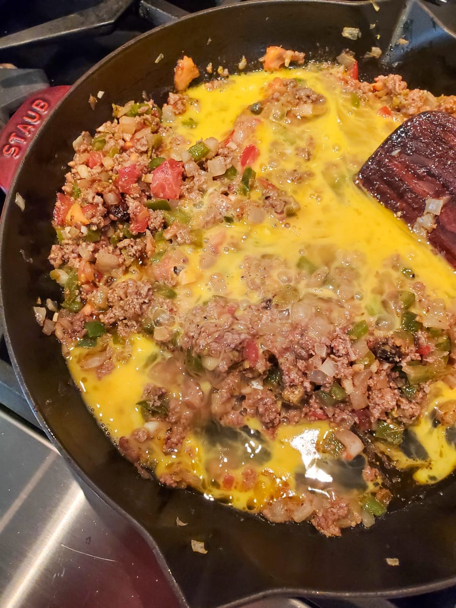 Egg being added to a skillet of seasoned beef.