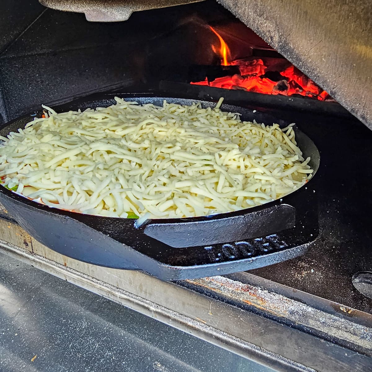 Cast iron pizza dip being placed in an Ooni pizza oven. 