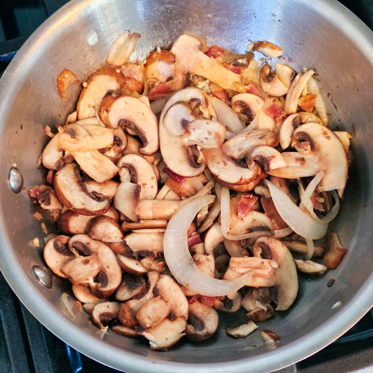 Mushrooms and onion cooking in a saucepan.
