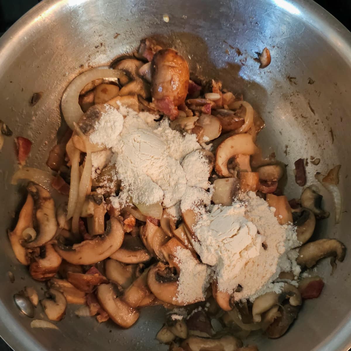 Flour added to a a saucepan of sautéed mushrooms and onion.