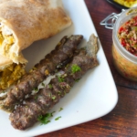 Lamb and Beef Kefta kebabs on a plate with shawarma wrap and shatta sauce.