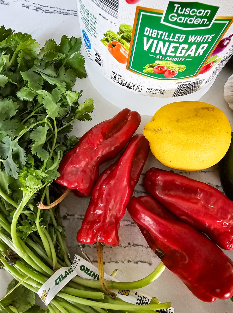 Alleppo peppers, white vinegar, lemon, and cilantro on a counter.