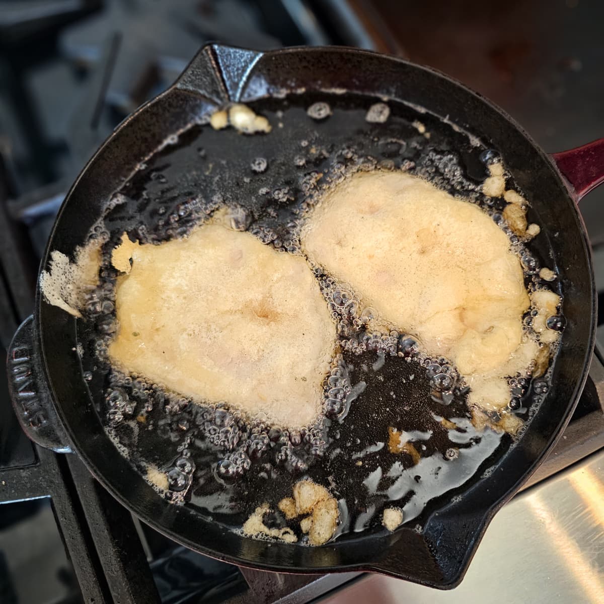 Tempura pork tenderloins frying in oil in a cast iron pan.